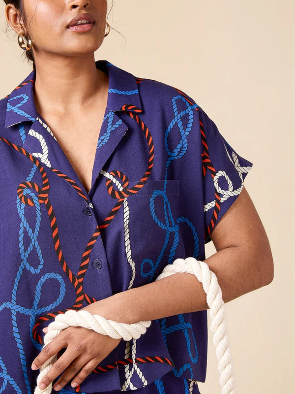 Person wearing a blue patterned shirt with ropes, holding a white rope.