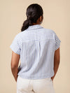 A woman shown from behind wearing a short-sleeve collared blouse with vertical light blue and white stripes, paired with white pants, against a solid beige background.