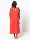 Woman wearing a coral dress made using a style arc Esther woven dress sewing pattern with bow details on a white background