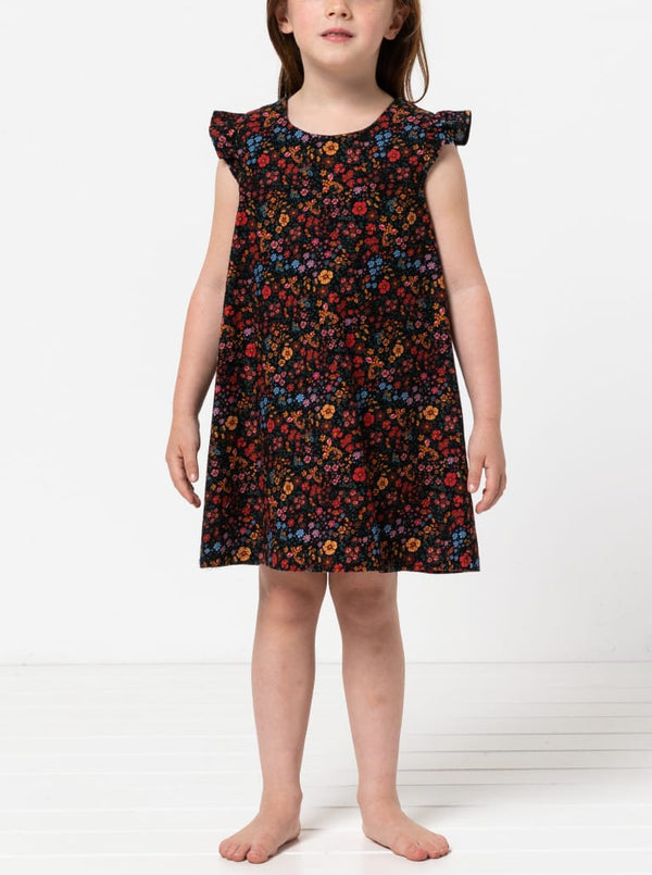 Young girl wearing a floral dress made using andie kids dress sewing patternon a white background