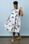 Woman wearing a blue and white floral dress made using Azure Dress, Skirt, and Top sewing pattern with yellow sandals against a light blue background