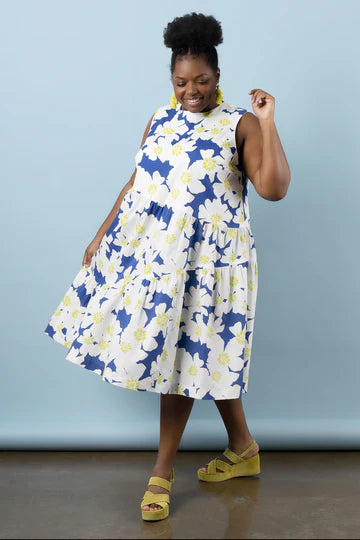 Woman wearing a blue and white floral dress made using Azure Dress, Skirt, and Top sewing pattern with yellow sandals against a light blue background