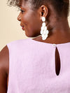 Woman wearing large white earrings with a light purple top on a beigemade using Azure Dress, Skirt, and Top sewing patternbackground