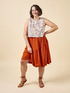 Woman wearing a sleeveless floral top and rust-colored skirt on a beige background