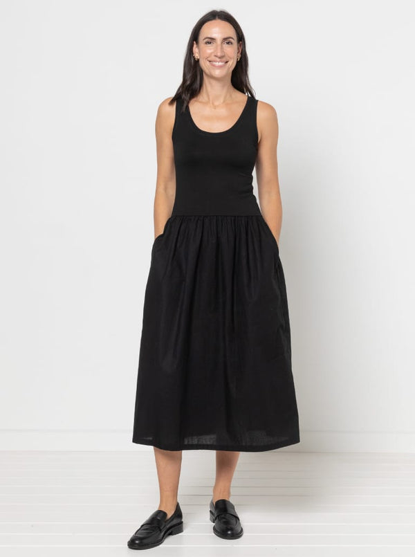 Woman wearing a black sleevelessCarter Dress made using StyleArc pattern with tee bodice and mid-calf linen skirt on a white background