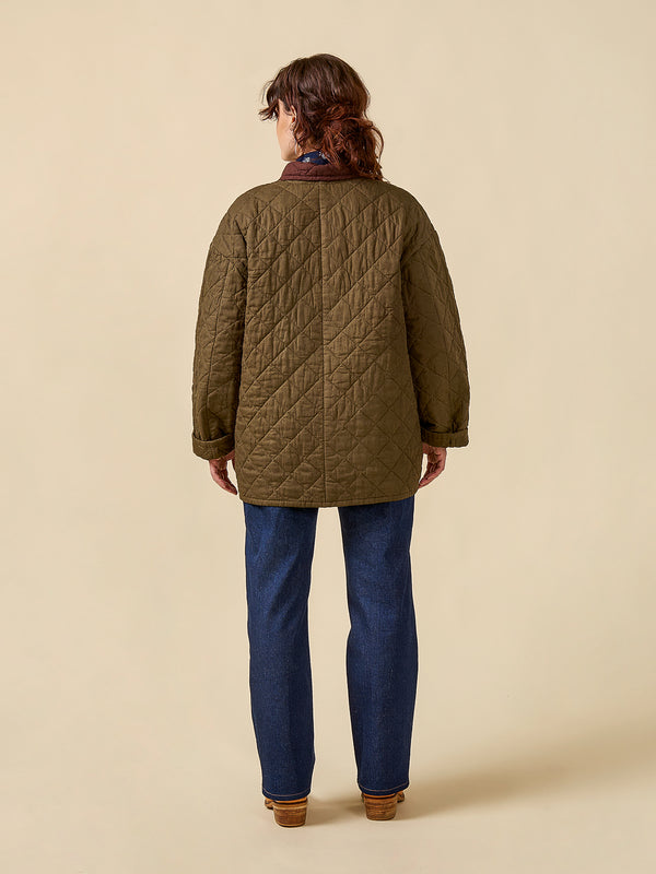 Person wearing a quilted jacket and blue jeans on a beige background