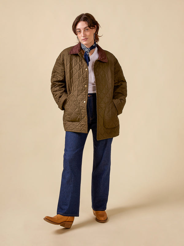Person wearing a quilted jacket, blue jeans, and brown shoes on a beige background