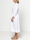 Person wearing a white dress against a plain background. the dress made of using Hampton Woven Dress Sewing Pattern – Mid-calf shirtdress with gathered skirt, curved waist, sleeve or sleeveless options, and inseam pockets.