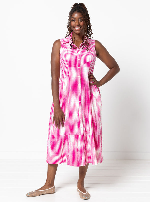 Woman wearing a pink checkered dress on a white background. The dress is made from the Hampton Woven Dress Sewing Pattern – a mid-calf shirtdress with a gathered skirt, curved waist, sleeve or sleeveless options, and inseam pockets.