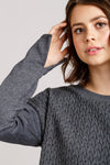 Woman wearing a gray textured sweater against a plain background