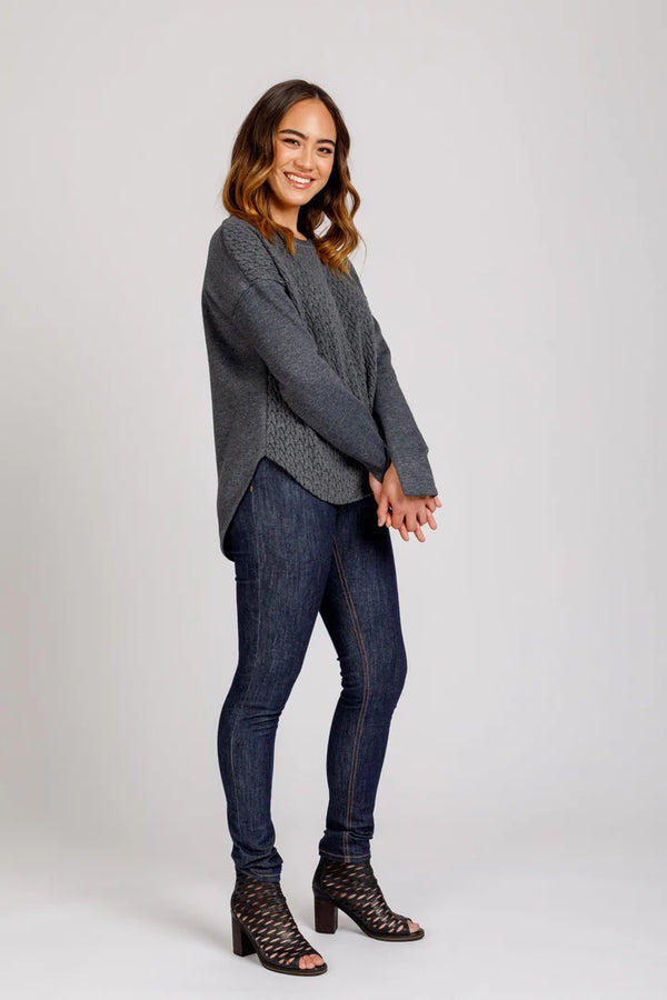Woman wearing a gray sweater and blue jeans on a white background