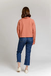 Person wearing a pink Jarrah sweater and blue jeans on a plain background