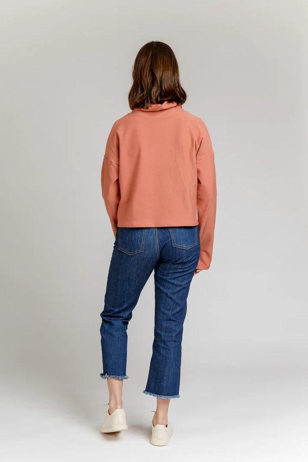 Person wearing a pink Jarrah sweater and blue jeans on a plain background