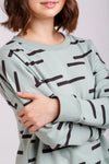 Person wearing a light green Jarrah sweaterwith brown abstract patterns on a plain background