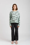 Woman wearing a light green sweater with black abstract patterns on a white background