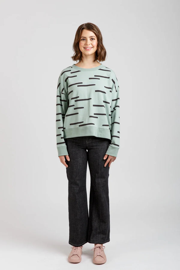 Woman wearing a light green sweater with black abstract patterns on a white background