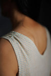 Close-up of a person wearing a sleeveless checkered dress made using The Lilian Sewing Pattern by Merchant & Mills with a blurred background