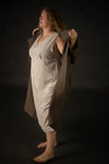 Person wearing a beige dress made using The Lilian Sewing Pattern by Merchant & Mills and coat against a dark background