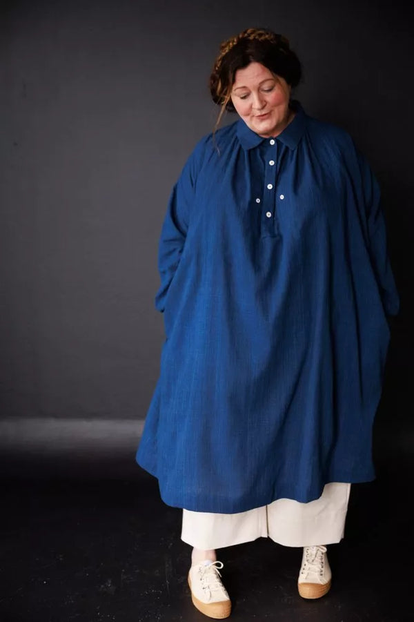 Person wearing a blue coat over a white outfit against a dark background