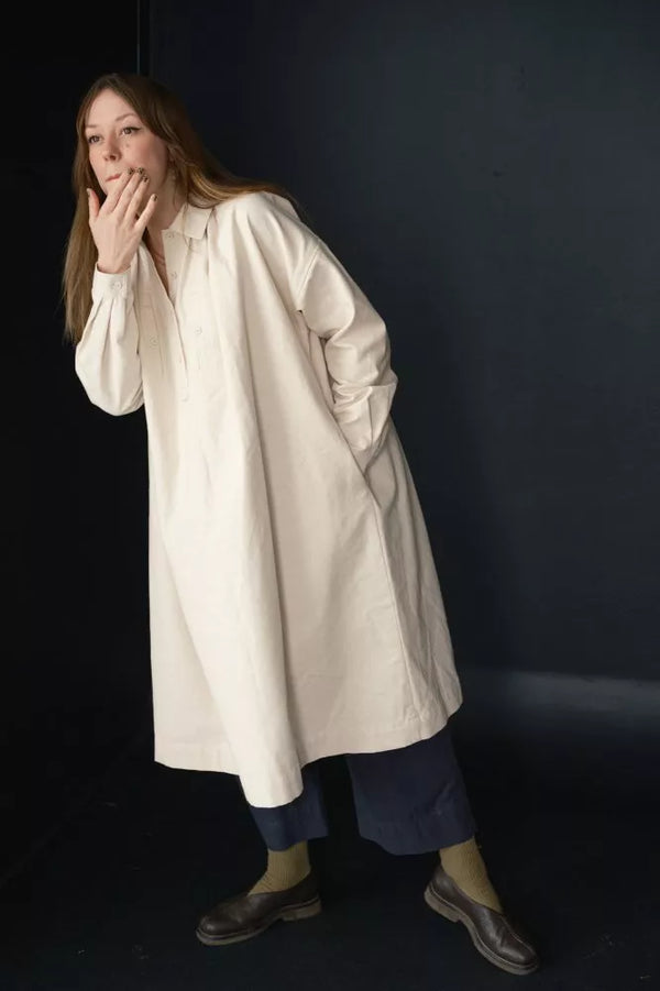 Person wearing a long white coat against a dark background