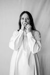 Black and white photo of a person wearing a long, light-colored garment against a plain background