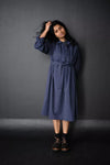Woman wearing a blue The Cawley Sewing Pattern by Merchant & Millsagainst a dark gray background