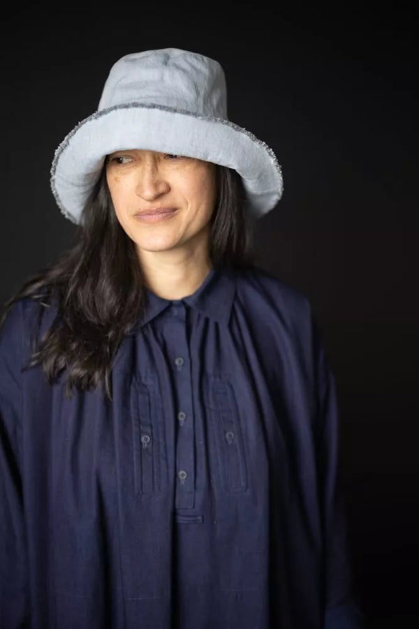 Person wearing a light gray bucket hat and dark blue shirt against a black background