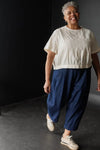 Woman wearing a white top top made using The Celeste Sewing Pattern by Merchant & Mills and blue pants against a black background