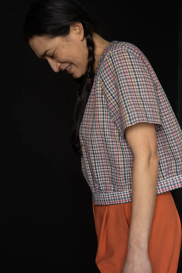 Person wearing a plaid top made using The Celeste Sewing Pattern by Merchant & Mills and orange pants against a black background