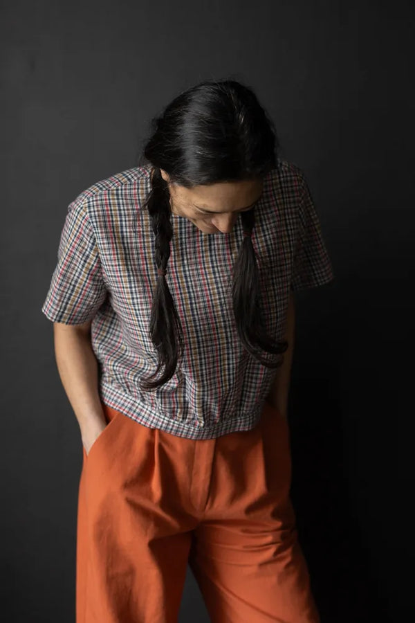 Person wearing a plaid top made using The Celeste Sewing Pattern by Merchant & Mills and orange pants against a dark background