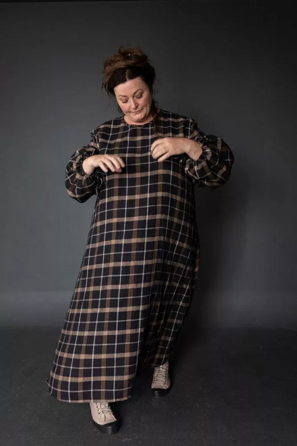 Person wearing a long plaid dress against a dark background