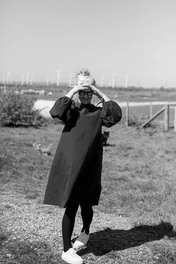 Person in a long coat standing in a field with wind turbines in the background