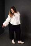Person wearing a white blouse and black pants on a dark background