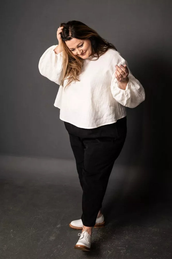Person wearing a white blouse and black pants against a dark background