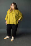 Woman wearing a mustard yellow blouse and black pantsmade using The Eve Trouser Sewing Pattern by Merchant & Mills – cropped tapered trousers with side zip and pleats against a gray background
