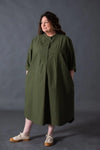 Woman wearing a green dress made using The Niven Sewing Pattern by Merchant & Millsagainst a gray background