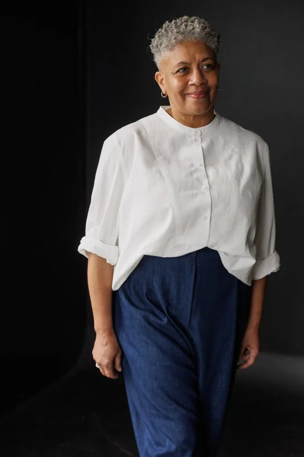 Person wearing a white blouse made using The Niven Sewing Pattern by Merchant & Mills and blue pants against a black background