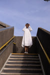 Person in a white dressstanding on a set of stairs with a clear blue sky.