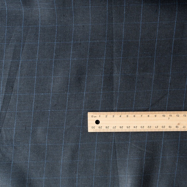 Close-up of Midnight Grid Herringbone Linen fabric with a deep navy hue, blue grid lines, and textured herringbone weave, suitable for tailored garments and home textiles.