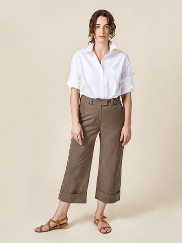 Woman wearing a white shirt and brown pants on a beige background