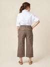 Woman wearing a white shirt and beige pants made of Rika Pants sewing pattern in cropped tailored style with hem cuffs and tabbed waistband against a beige background