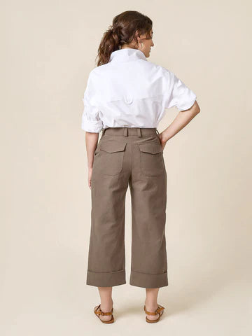 Woman wearing a white shirt and beige pants made of Rika Pants sewing pattern in cropped tailored style with hem cuffs and tabbed waistband against a beige background