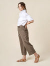 Woman wearing a white shirt and brown pantsmade of Rika Pants sewing pattern in cropped tailored style with hem cuffs and tabbed waistbandon a beige background