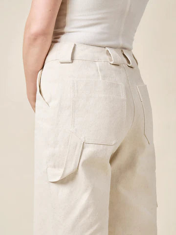 Beige pantsmade of Rika Pants sewing pattern in cropped tailored style with hem cuffs and tabbed waistbandworn by a person on a beige background