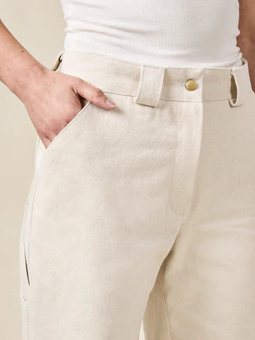 Beige pants made of Rika Pants sewing pattern in cropped tailored style with hem cuffs and tabbed waistbandwith a white top on a neutral background