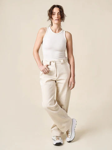 Woman wearing a white sleeveless top and beige pants against a plain background
