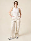 Woman wearing a white tank top and beige pants made of Rika Pants sewing pattern in cropped tailored style with hem cuffs and tabbed waistbandagainst a plain background