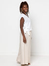 Woman wearing a white sleeveless top made using Rumi Top Sewing Patternand beige pants against a white background