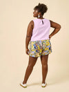 Woman wearing a light purple sleeveless top and colorful floral shorts made using Sepia Pants and Shorts sewing patternon a beige background