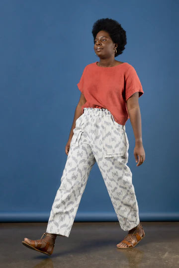 Woman wearing a coral top and white patterned pants made using Sepia Pants and Shorts sewing patternagainst a blue background